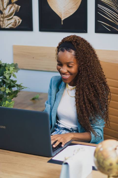 mulher negra empreendedora sorri olhando para computador sentada em mesa de escritório'