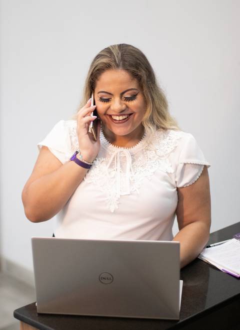 mulher loira segura telefone sorrindo enquanto olha para computador'