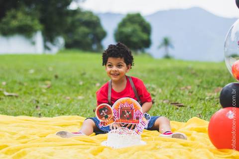 criança menino de cabelo cacheado no gramado posa sentado para ensaio fotográfico infantil '