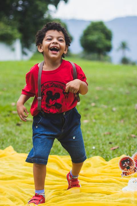 menino de cabelo cacheado brinca correndo no gramado posando para foto '