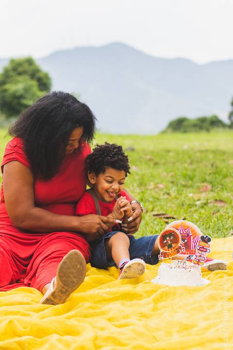 mãe mulher negra com filho pequeno de cabelo cacheado no gramado ensaio fotográfico infantil '
