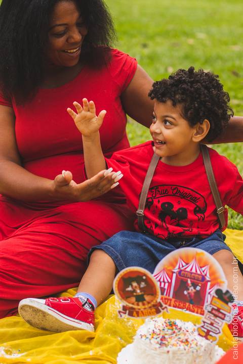 mãe mulher negra com filho pequeno de cabelo cacheado no gramado ensaio fotográfico infantil '