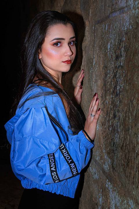 A modelo está encostada em um muro de pedra e olhando para frente'