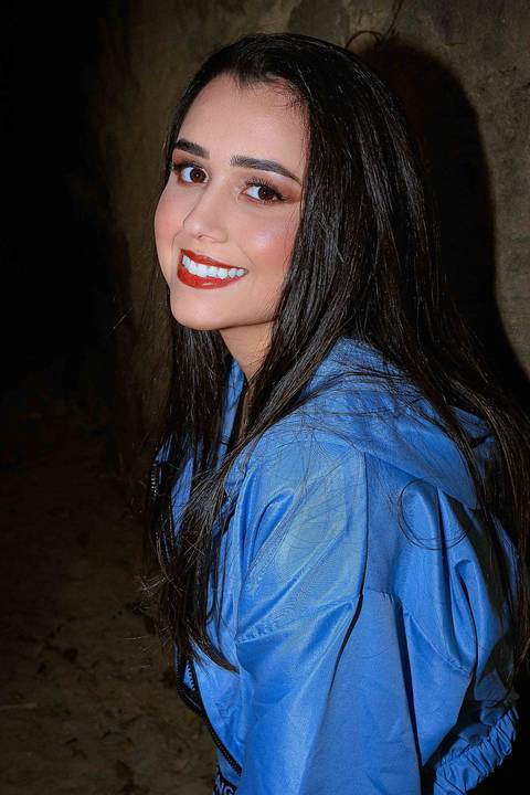 A modelo está encostada em um muro de pedra, abaixada e olhando para frente'