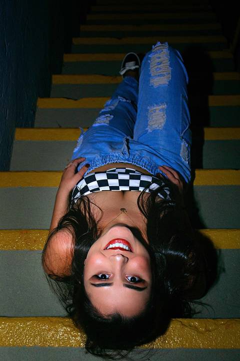 A modelo está sentada na escada apoiando no degrau com o cotovelo, a foto foi tirada de cima'