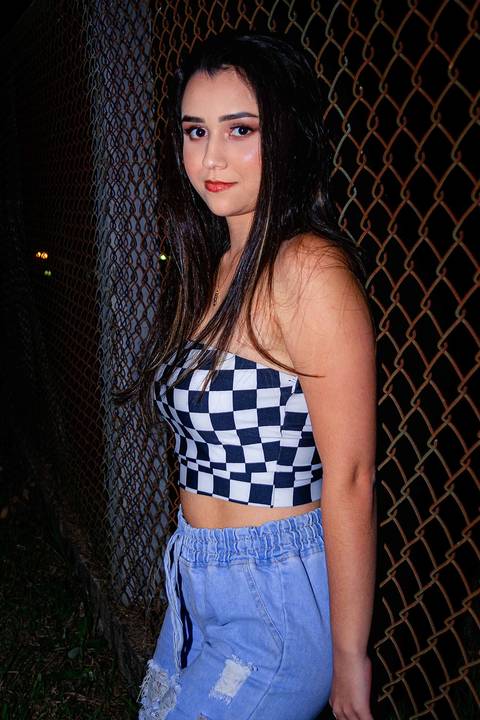 foto tirada com a modelo apoiando em uma cerca, ela está na frente da cerca '