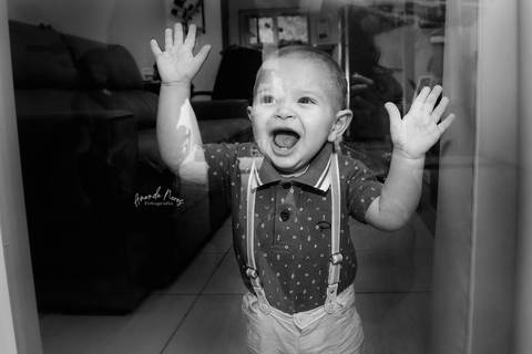 Criança com as mãos apoiada no vidro da porta e rindo'