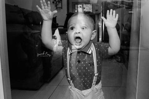 Criança com as mãos apoiada no vidro da porta com cara de surpresa '