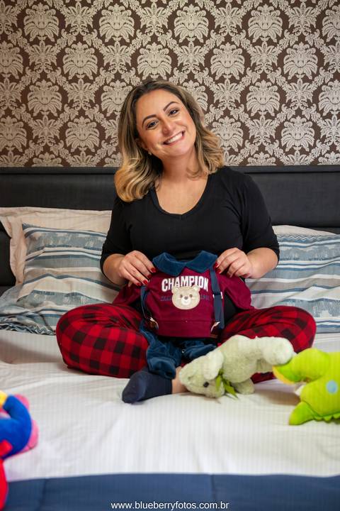 Mãe gravida segurando roupinha de bebe'
