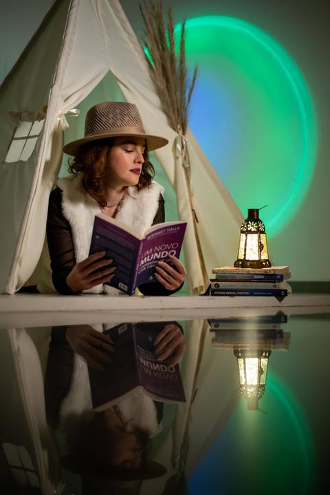 Mulher usado chapéu, com livro na mão e sentada ao lado de uma lamparina'