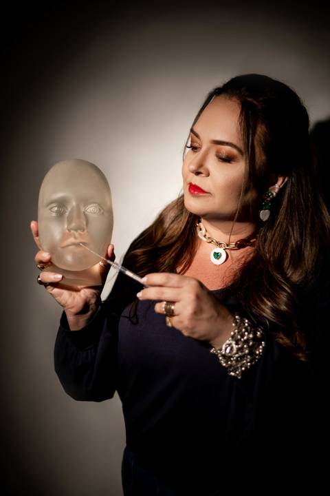 Mulher segurando uma mascara com formato de um rosto'