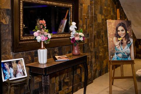 Mesa com dois vasos e com flores sobre ela quadros de fotos e um espeho na parede'