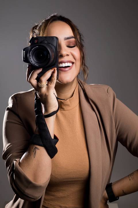 Mulher sorrindo com camera fotografica nas mãos usando roupa na cor terra'
