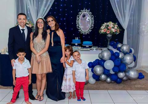 foto em familia em uma festa de 15 anos toda decorada de azul com baloes azuis e cortina branca e espelho no fundo com um tecido azul escuro com pisca pisca azul'