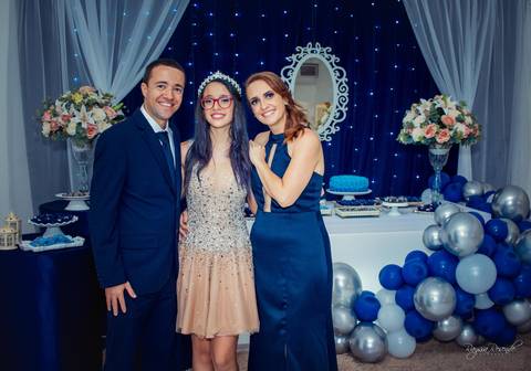 foto em familia em uma festa de 15 anos toda decorada de azul com baloes azuis e cortina branca e espelho no fundo com um tecido azul escuro com pisca pisca azul'