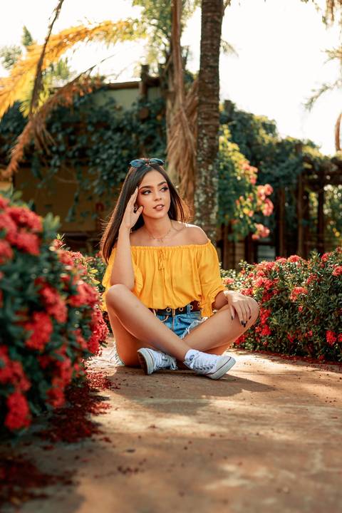 garota de 15 anos de blusa amarela e short jeans no meio das flores'