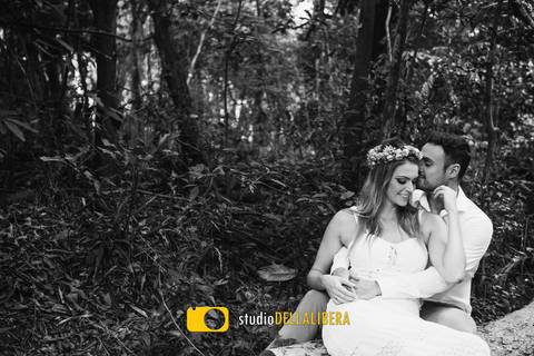 Sessão pre-weeding, foto em PB, com os noivos sentados em arvore caída em bosque com muito verde'