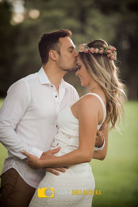 Noivos Carol e Rodrigo em sessão pre-wedding com noivo dando beijo na testa da noiva com cenário arvores ao fundo'