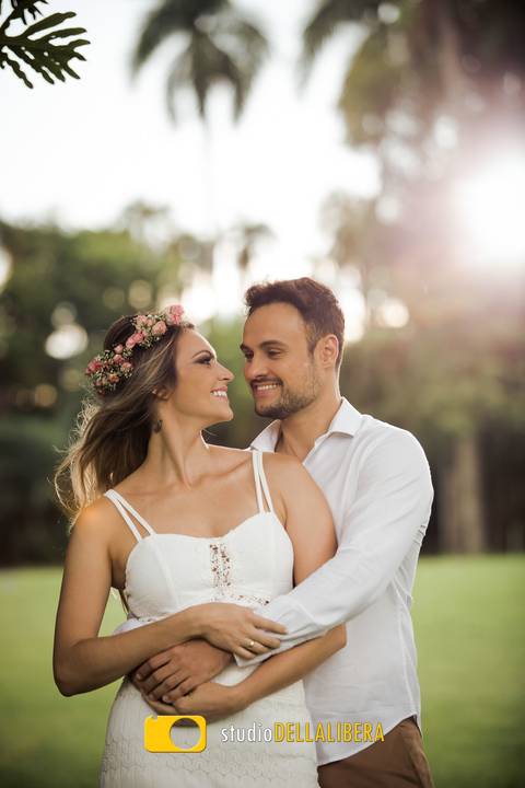 Noivos Carol e Rodrigo trocando olhares, Rodrigo abraçando a noiva Carol os dois com vestes brancas, a noiva com tiara de flores do campo e vestido branco casual e noivo com camisa branca.'