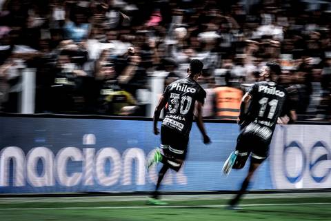 Lucas Braga comemorando gol com a torcida na Vila Belmiro. Técnica aplicada de panning.'