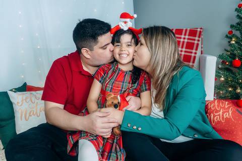 Ensaio de Natal em Família em Piraquara e Curitiba Paraná. Menina com seus pais no cenário de natal com enfeites e arvore de natal.'