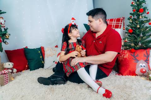 Ensaio de Natal em Família em Piraquara e Curitiba Paraná. Menina com seu pai no cenário natalino com enfeites e arvore de natal.'