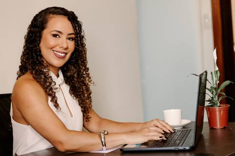 ensaio em casa fotos corporativas bom despacho renata bridges blazer marrom blusa branca cabelo cacheado make dia xícara branca computador quarto notebook look preto'