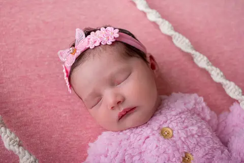 Fotografia de bebê no ensaio newborn. A bebê está usando uma roupa de ursinho cor de rosa, com uma faixinha de flores e borboletas. Foto feita pela fotógrafa Carol Zimmermann na cidade de São José, SC.'