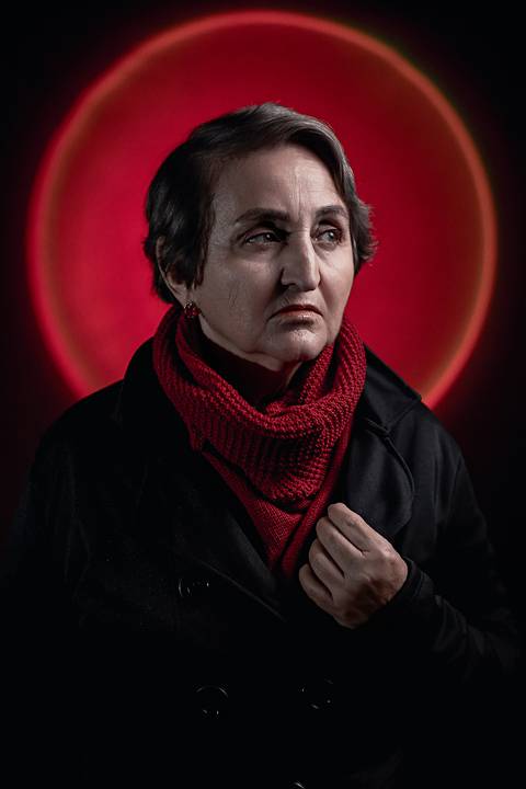 Imagem de mulher na faixa dos 50 anos olhando para o lado usando uma jaqueta preta.'