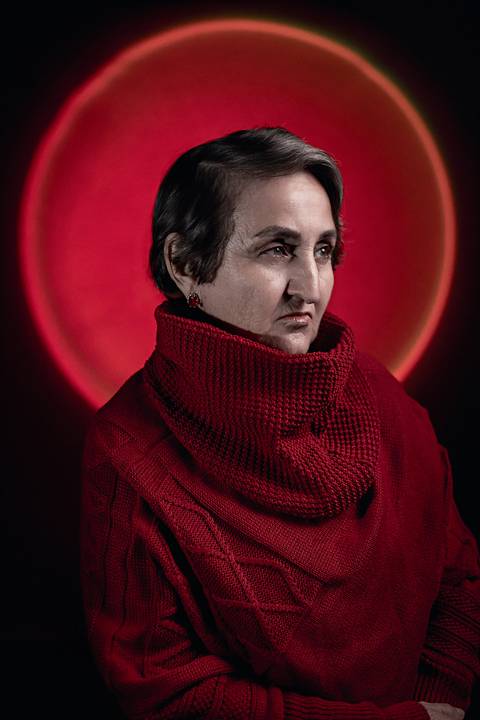 Imagem de mulher na faixa dos 50 anos com um olhar sério usando uma blusa de frio de gola alta.'