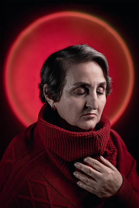 Imagem de mulher na faixa dos 50 anos olhos fechados usando uma blusa de frio de gola alta.'