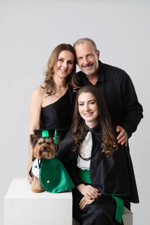 Retrato oficial de formatura em Medicina. Maria Eduarda vestindo beca tradicional, capelo e segurando o diploma da faculdade.'