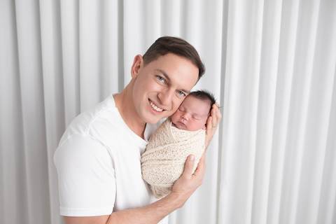 Retrato de pai e filho no ensaio newborn. O papai Marcos segurando o bebê Rafael nos braços, transmitindo orgulho, proteção e amor.'