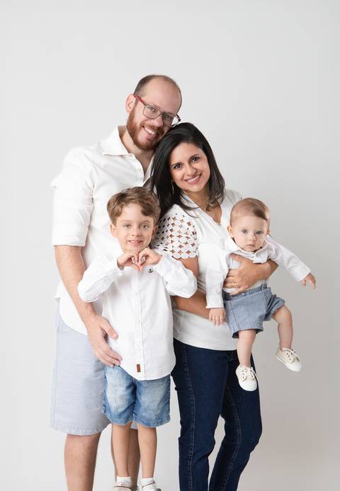 Retrato de família com bebê de 6 meses em Brasília. A mamãe Naiá, o papai e o irmão Miguel reunidos com o pequeno Matheus em cenário minimalista com fundo claro.'
