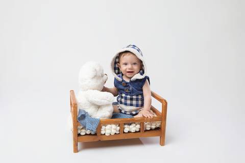 Desenvolvimento saudável e descobertas naturais na infância. O pequeno Matheus aos 6 meses interagindo de forma lúdica com ursinho de pelúcia em mini cama de madeira.'