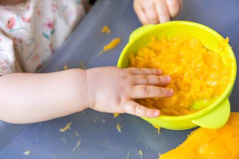 Introdução alimentar e descobertas sensoriais na infância. A bebê Cecília aos 8 meses experimentando manga em momento espontâneo e lúdico com frutas.'