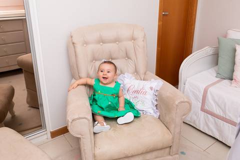 Desenvolvimento saudável de bebê de 8 meses. Cecília sorrindo na poltrona em registro afetivo e acolhedor dentro do ambiente familiar.'