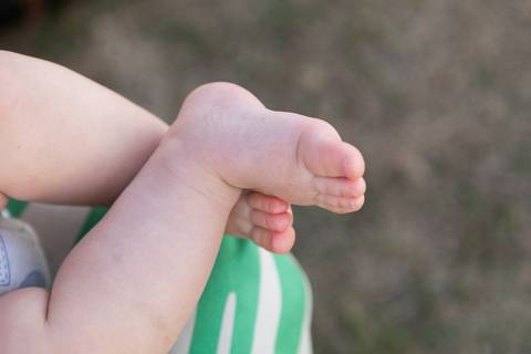 Detalhes sensíveis e pureza da infância ao ar livre. Cecília descalça no gramado brincando e sorrindo em um dia de sol e lazer em família.'