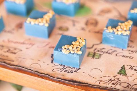 Detalhes da decoração temática de aniversário de 9 anos inspirada no livro Percy Jackson. Registro lúdico de doces personalizados e bolo do Acampamento Meio-Sangue em Brasília.'