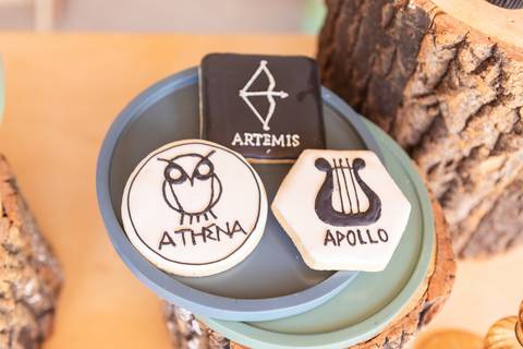 Detalhes da decoração temática de aniversário de 9 anos inspirada no livro Percy Jackson. Registro lúdico de doces personalizados e bolo do Acampamento Meio-Sangue em Brasília.'