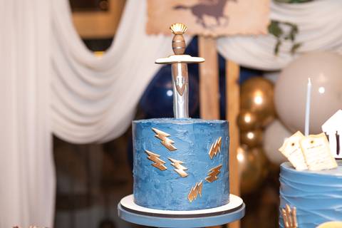 Detalhes da decoração temática de aniversário de 9 anos inspirada no livro Percy Jackson. Registro lúdico de doces personalizados e bolo do Acampamento Meio-Sangue em Brasília.'