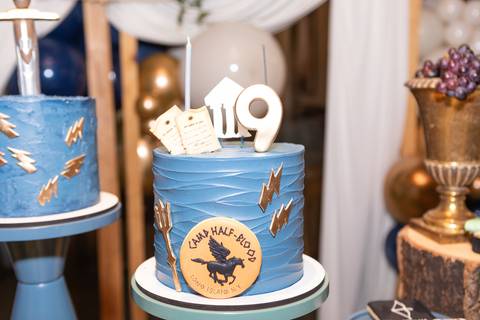 Detalhes da decoração temática de aniversário de 9 anos inspirada no livro Percy Jackson. Registro lúdico de doces personalizados e bolo do Acampamento Meio-Sangue em Brasília.'