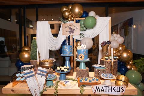 Detalhes da decoração temática de aniversário de 9 anos inspirada no livro Percy Jackson. Registro lúdico de doces personalizados e bolo do Acampamento Meio-Sangue em Brasília.'