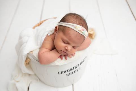 Bem-estar infantil e a delicadeza dos primeiros dias de vida. A bebê Ísis descansando de forma segura em cenário minimalista claro.'