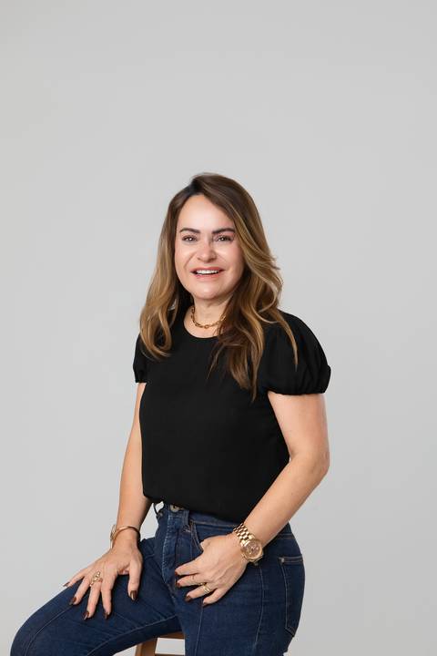 Retrato feminino em estúdio. A mamãe Glêdes sorrindo com look casual preto e jeans em uma composição clean e atemporal.'