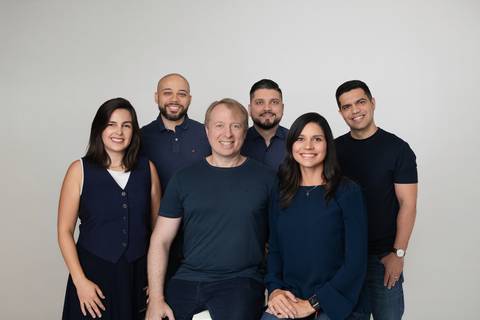 Foto de equipe corporativa em estúdio. Os fundadores Mariana e Vincenzo reunidos com o time de consultores da VP Concursos em imagem institucional com trajes coordenados.'