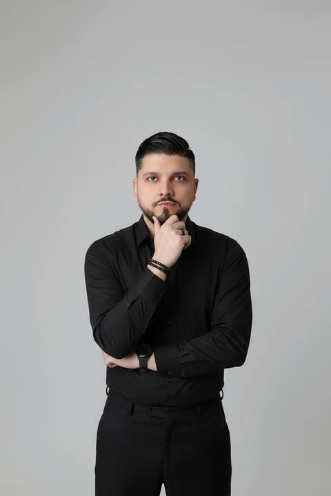 Retrato profissional masculino em estúdio. Consultor Vitor em pose focada com camisa preta em cenário minimalista claro.'
