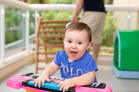 Desenvolvimento motor e estímulos lúdicos na infância. A bebê Cecília aos 10 meses interagindo com brinquedo musical em ambiente protegido.'