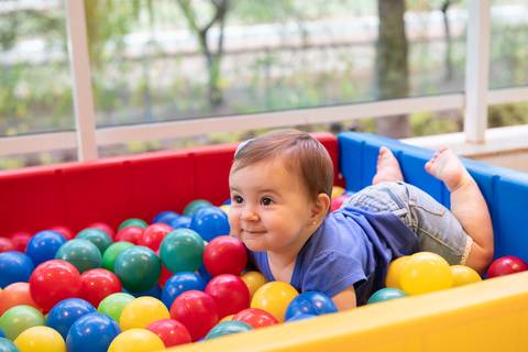 Momentos lúdicos e pura diversão na infância. Cecília sorrindo em meio às bolinhas coloridas, focando no bem-estar e na alegria do bebê.'