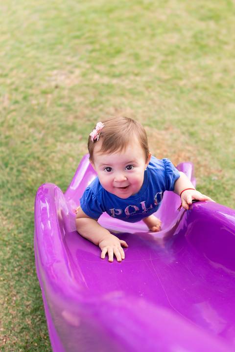 Autonomia e bem-estar infantil em atividades de lazer. Cecília descendo de forma divertida pelo escorregador colorido no gramado.'
